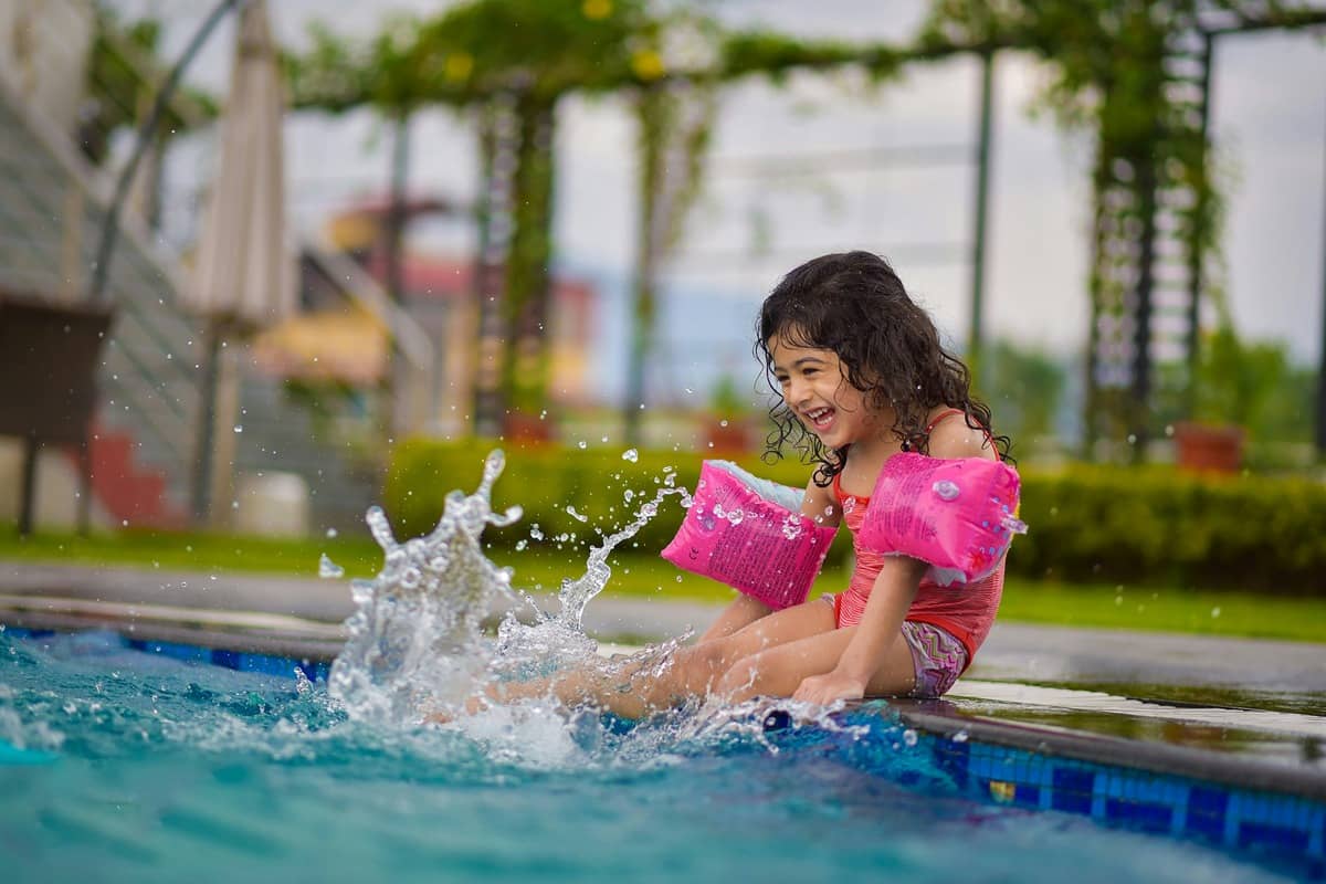 A parent watching a young child learn to swim confidently in a shallow pool at an Everyone Swims lesson